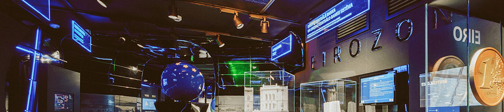 Latvijas Bankas zināšanu centrs. Tumši zila telpa ar dažādiem monitoriem un grafikām.
